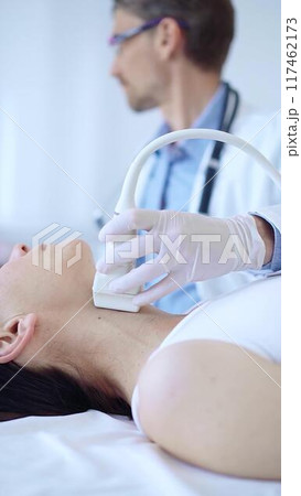 Doctor man wearing white protective gloves is using ultrasound machine to examine neck of female patient in hospital. Medicine, thyroid gland health 117462173