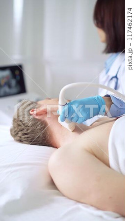 Doctor woman with blue medical gloves performing neck ultrasound exam on male patient 117462174