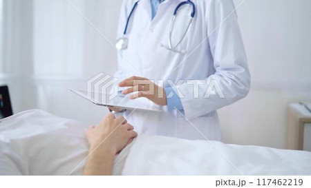 Doctor consulting patient with digital tablet in hospital room. Healthcare professional providing care 117462219