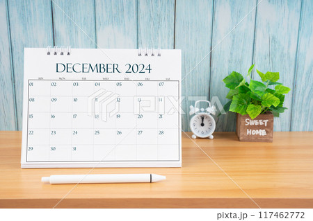 December Monthly desk calendar for 2024 year and alarm clock on table. 117462772