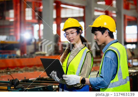 man and woman industrial engineers wear hard hats and uniform using laptop 117463139