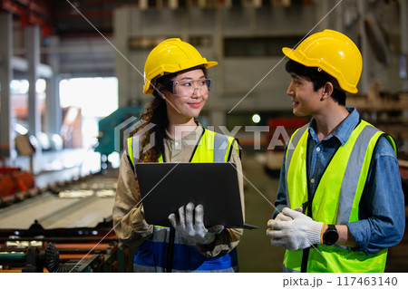 man and woman industrial engineers wear hard hats and uniform using laptop 117463140