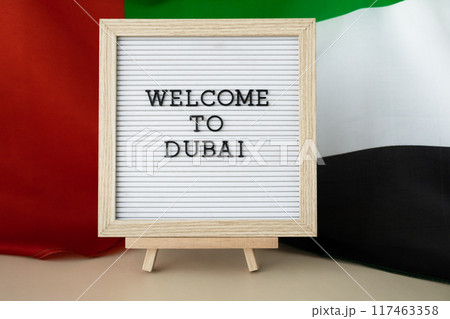 Frame text WELCOME TO DUBAI on background of waving UAE flag made from silk. United Arab Emirates flag with concept of tourism and traveling. Inviting greeting card, advertisement 117463358