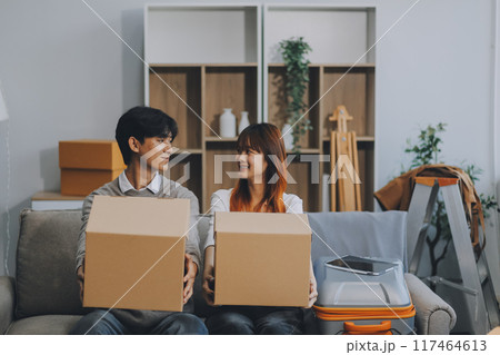 Young Asian couple relocating to a new house, joyfully packing and unpacking belongings. Expertise in moving, packing, togetherness, and creating a new home together. Young Asian couple relocating to a new house, joyfully packing and unpacking belongings. Expertise in moving, packing, togetherness, and creating a new home together. 117464613