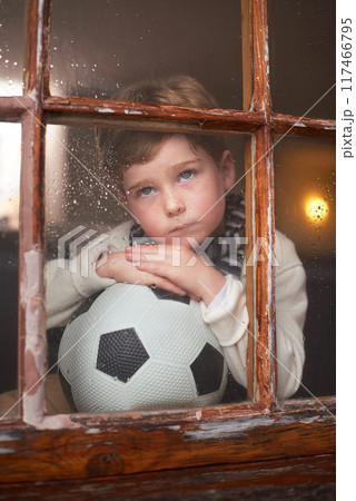 Thinking, sad and kid by window with soccer ball for playing outdoor, frustrated and waiting for rain. Bored, lonely and young boy by glass with football for mental health and psychology in home 117466795