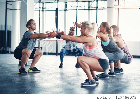 People, personal trainer and squating exercise for fitness in health club, wellness workout and strength for muscles. Challenge, body and balance for core, determination and instructor talking 117466975