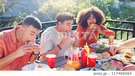 Friends, group and eating hamburger outdoor on terrace with hunger, reunion and social event in summer. People, barbecue and lunch on patio with food, diversity or celebration with bonding and drinks 117466984
