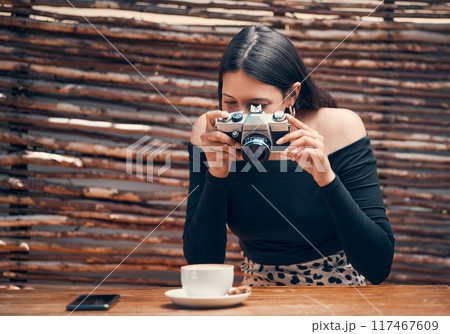Stylish, trendy and creative food influencer taking a picture with a camera of a cup of coffee for her blog in a cafe shop. Young female content creator taking a photo for her blog website at a cafe 117467609
