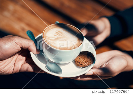 Closeup of hands holding and giving a cappuccino or flat white to a customer at a cafe. Hot beverage with creative plant image in milk foam. A morning coffee drink made by a barista in a restaurant. Closeup of hands holding and giving a cappuccino or flat white to a customer at a cafe. Hot beverage with creative plant image in milk foam. A morning coffee drink made by a barista in a restaurant. 117467664