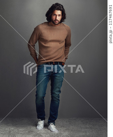 Serious, portrait and man with fashion in studio for elegant, style and comfortable winter jeans clothes. Cool, male person and trendy jersey, designer wardrobe or hands in pocket on grey background 117467691