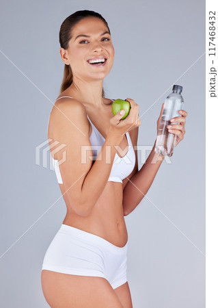 Portrait, woman and apple with water for healthy diet, fitness and nutrition in grey studio background. Wellness, female person and fruit happy with drink for organic meal, snack or vegan eating 117468432