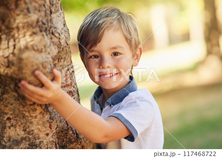 Boy, hide and play by tree for portrait in park for games, adventure and outdoor for playing in summer. Child, nature and shy smile in forest for holiday, vacation and freedom for growth in Canada 117468722