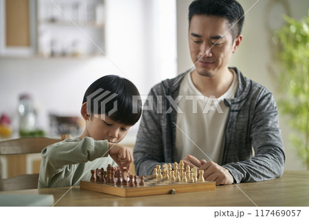 young asian father playing chess with son at home 117469057