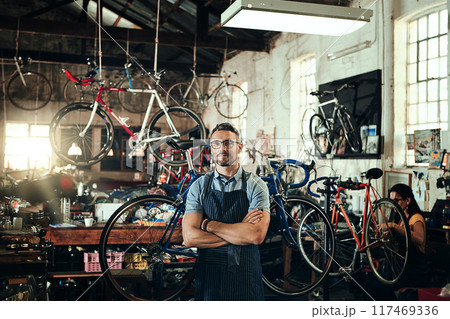 Man, portrait and arms crossed at work in bike repair shop or maintenance garage. Bicycle, mechanic and service with a professional handyman for startup, small business and workshop for fixing 117469336