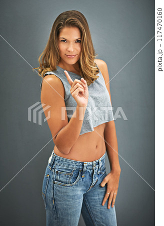 Woman, fashion and portrait in studio with finger for confidence, positive attitude and denim clothes. Female person, calm or relax in grey background for cool, trendy and casual style in USA 117470160