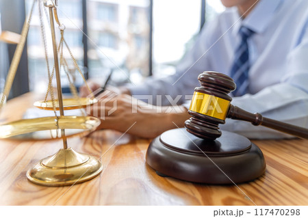 Close up of justice scale and court gavel with blurred working male lawyer in background Close up of justice scale and court gavel with blurred working male lawyer in background 117470298