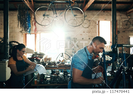 Bicycle technician, repair and working in shop with frame, chain and tools for maintenance or cycling. Mechanic, bike and teamwork in workshop as handyman for gear, inspection and safety with woman 117470441