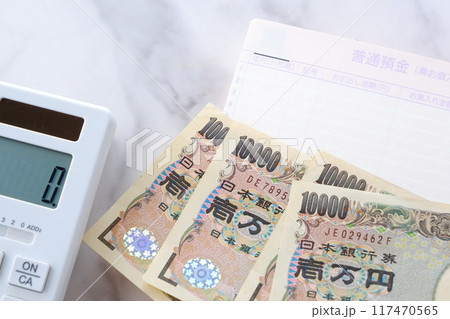 テーブルの上に開いた状態で置かれた銀行の預金通帳と、1万円札、電卓 117470565