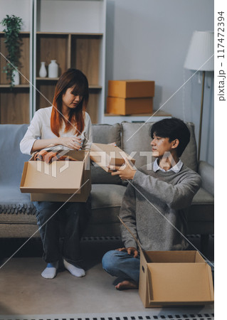 Young Asian couple relocating to a new house, joyfully packing and unpacking belongings. Expertise in moving, packing, togetherness, and creating a new home together. 117472394