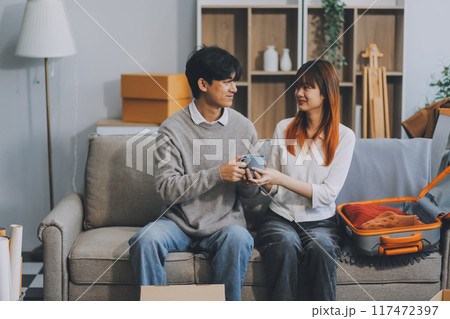 Young Asian couple relocating to a new house, joyfully packing and unpacking belongings. Expertise in moving, packing, togetherness, and creating a new home together. 117472397