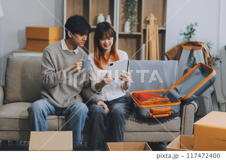 Young Asian couple relocating to a new house, joyfully packing and unpacking belongings. Expertise in moving, packing, togetherness, and creating a new home together. 117472400