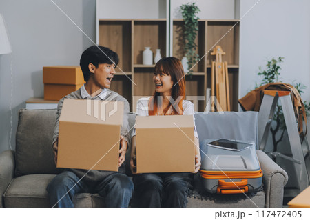 Young Asian couple relocating to a new house, joyfully packing and unpacking belongings. Expertise in moving, packing, togetherness, and creating a new home together. 117472405