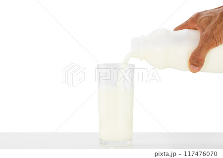 Hand holding bottle of milk pouring into glass on white table on white background 117476070