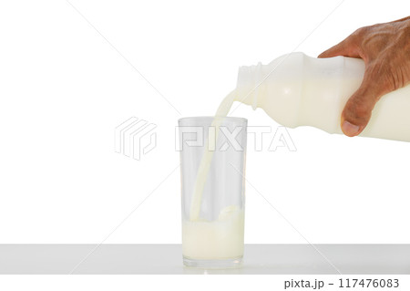 Hand holding bottle of milk pouring into glass on white table on white background Hand holding bottle of milk pouring into glass on white table on white background 117476083