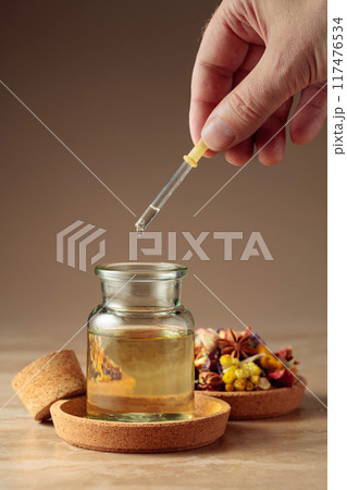Dropping essential oil or herbal tincture into a glass bottle. Dropping essential oil or herbal tincture into a glass bottle. 117476534