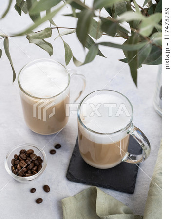 Two cappuccino or latte with milk foam in glasses on a light background with coffee beans Two cappuccino or latte with milk foam in glasses on a light background with coffee beans 117478289