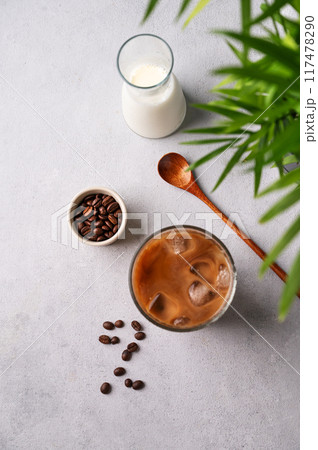 Iced coffee latte in a glass with milk on a light background with coffee beans, palm leaf and spoon 117478290