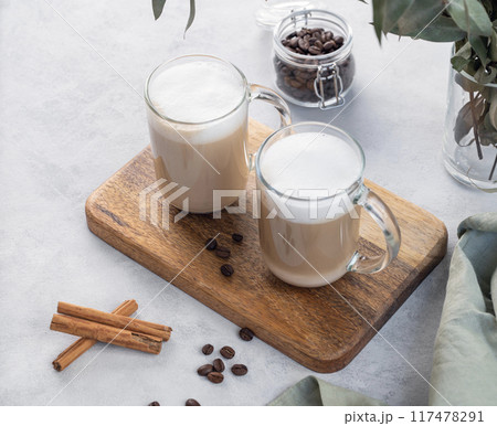 Two cappuccino or latte with milk foam in glasses on a light background with coffee beans 117478291