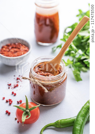 Hot sauce adjika. Homemade appetizer with pepper and tomatoes in a jar on light background Hot sauce adjika. Homemade appetizer with pepper and tomatoes in a jar on light background 117478500