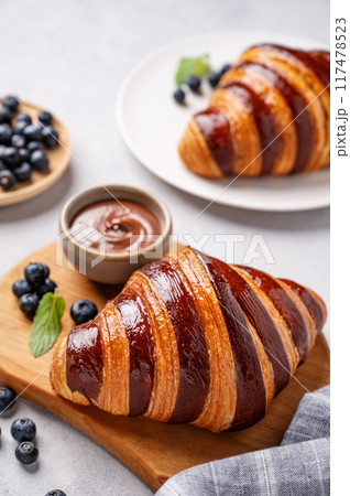 Fresh croissants with chocolate on a cutting board on a light background with a blueberries close up 117478523