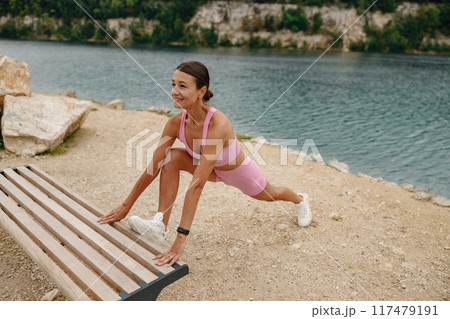 A woman is stretching by the beautiful water while wearing her stylish activewear outfit A woman is stretching by the beautiful water while wearing her stylish activewear outfit 117479191