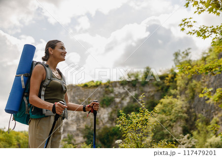 A Young Woman Enjoying Hiking in Beautiful Nature, Carrying a Backpack and Trekking Poles A Young Woman Enjoying Hiking in Beautiful Nature, Carrying a Backpack and Trekking Poles 117479201