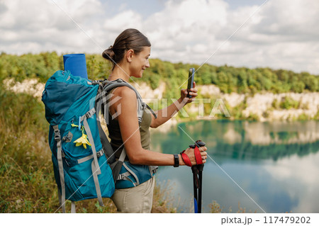 A Hiker is Enjoying a Relaxing Break at a Scenic Lake While Using a Smartphone to Capture the Moment A Hiker is Enjoying a Relaxing Break at a Scenic Lake While Using a Smartphone to Capture the Moment 117479202