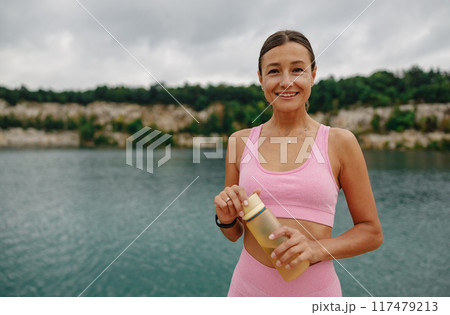 Active Lifestyle A Young Woman Enjoying Time by the Water While Holding a Water Bottle Active Lifestyle A Young Woman Enjoying Time by the Water While Holding a Water Bottle 117479213