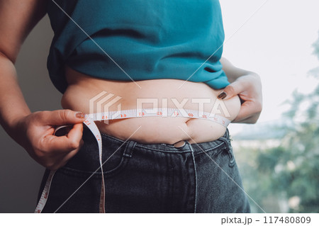 fat woman, fat belly, chubby, obese woman hand holding excessive belly fat with measure tape, woman diet lifestyle concept 117480809