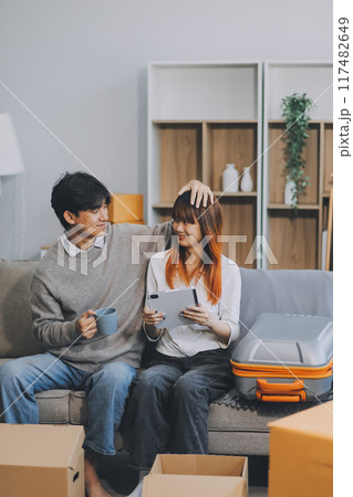 Young Asian couple relocating to a new house, joyfully packing and unpacking belongings. Expertise in moving, packing, togetherness, and creating a new home together. Young Asian couple relocating to a new house, joyfully packing and unpacking belongings. Expertise in moving, packing, togetherness, and creating a new home together. 117482649