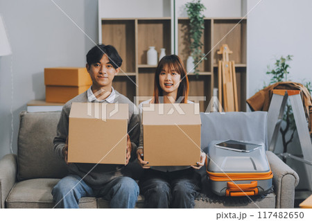 Young Asian couple relocating to a new house, joyfully packing and unpacking belongings. Expertise in moving, packing, togetherness, and creating a new home together. Young Asian couple relocating to a new house, joyfully packing and unpacking belongings. Expertise in moving, packing, togetherness, and creating a new home together. 117482650