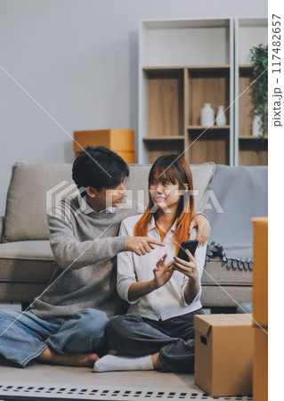 Young Asian couple relocating to a new house, joyfully packing and unpacking belongings. Expertise in moving, packing, togetherness, and creating a new home together. 117482657