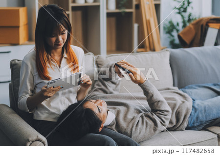 Young Asian couple relocating to a new house, joyfully packing and unpacking belongings. Expertise in moving, packing, togetherness, and creating a new home together. 117482658