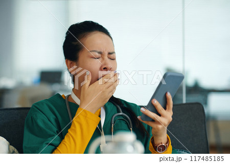 Yawning Medical Professional Holding Smartphone 117485185