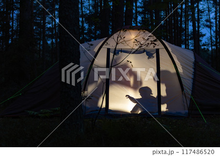 Children making shadow puppets in a camping tent at night 117486520