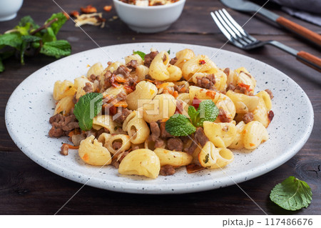 Stewed pasta with minced beef and vegetables, macaroni in Navy style on a plate. Dark wooden background. 117486676