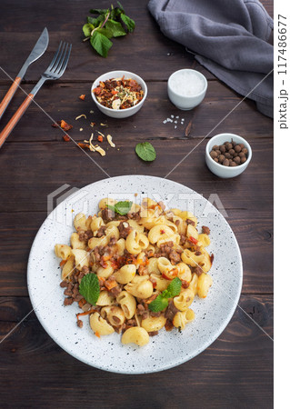 Stewed pasta with minced beef and vegetables, macaroni in Navy style on a plate. Dark wooden background. Copy space. 117486677