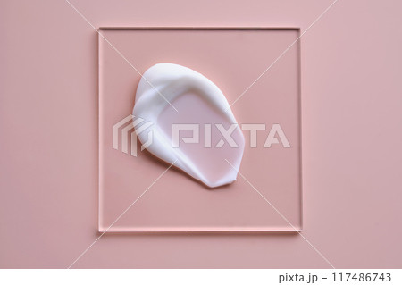 A smear of white cream on a square transparent stand on a pink background. A smear of white cream on a square transparent stand on a pink background. 117486743