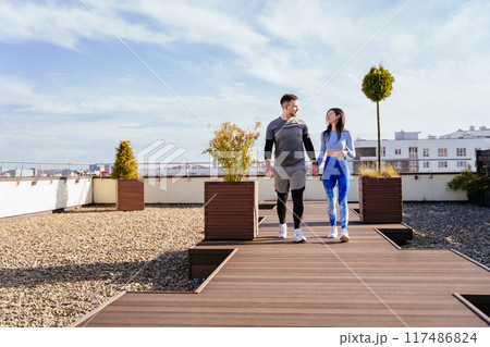Friends meeting on rooftop terrace in summer overlooking the city. Man and woman, couple exercising and relaxing taking break on rooftop. wide angle 117486824