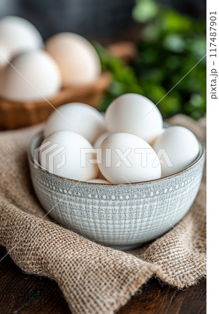 A rustic bowl filled with white and brown eggs on a textured burlap surface 117487901